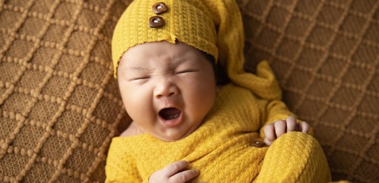 Newborn baby dressed in a yellow hat and top yawning