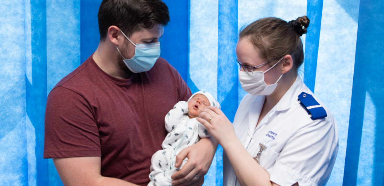 A dad holding his baby with a midwife.