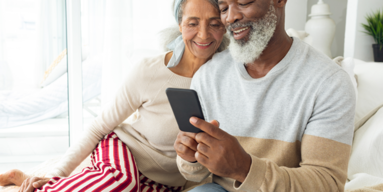 A man and a woman sat on a sofa smiling and looking at a mobile phone